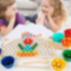 Two children smiling while playing the wooden bead board game with sorting cups.