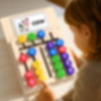 A young child sitting at a table is learning with a wooden Montessori alphabet board surrounded by word cards.