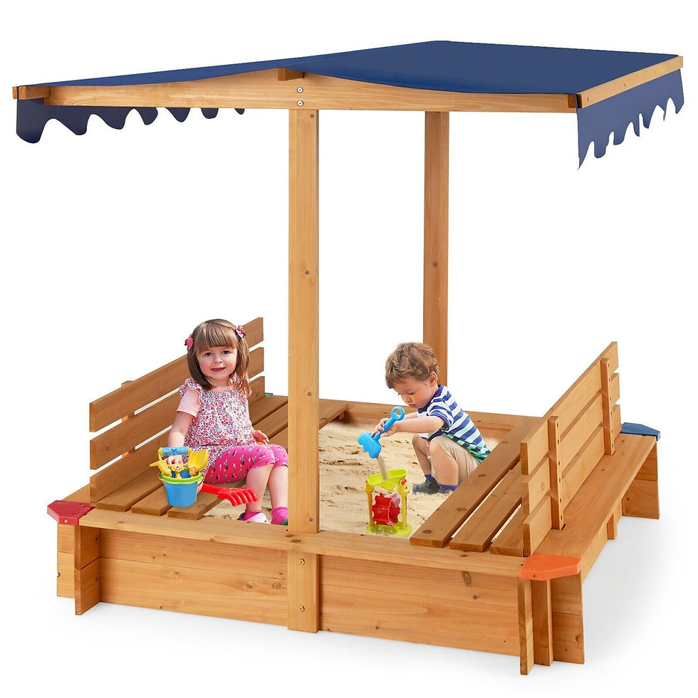 Two toddlers play in a wooden sandbox with a blue canopy; one scoops sand while the other smiles holding toys.