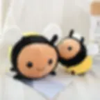 A large and a small cylindrical bee plush toy sitting side-by-side on a desk.