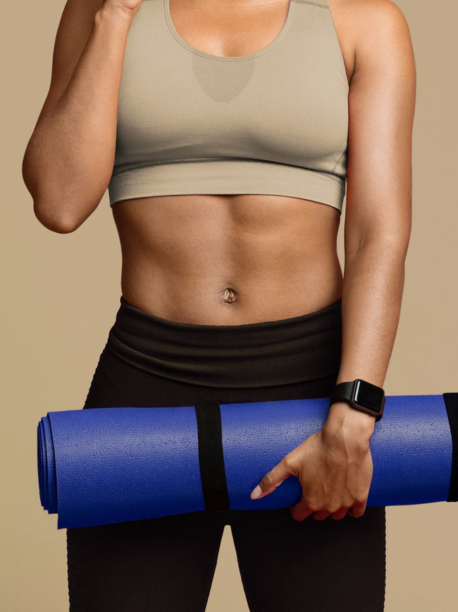 Woman in fitness wear holding a rolled blue yoga mat
