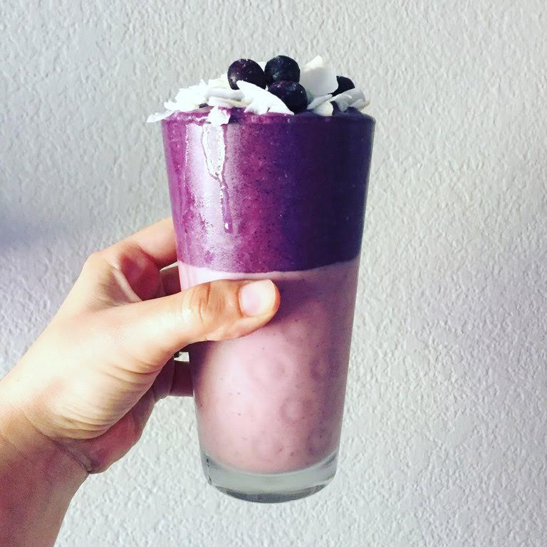 Hand holding a purple and pink smoothie