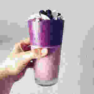 Hand holding a purple and pink smoothie