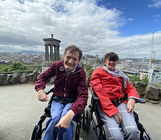 An image of two smiling people sat in wheelchairs with a view of a city.