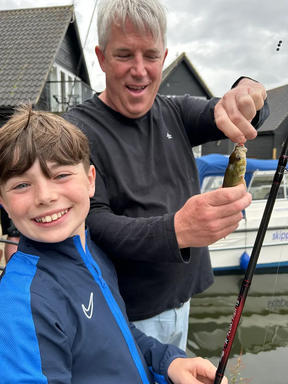 Father and son holding a fish together during a Norfolk Broads fishing lesson.