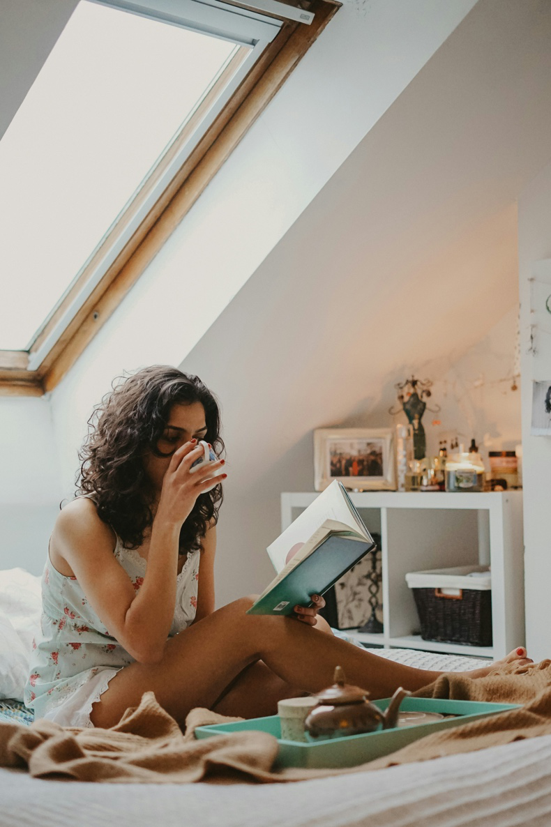 A woman is reading a book and drinking tea