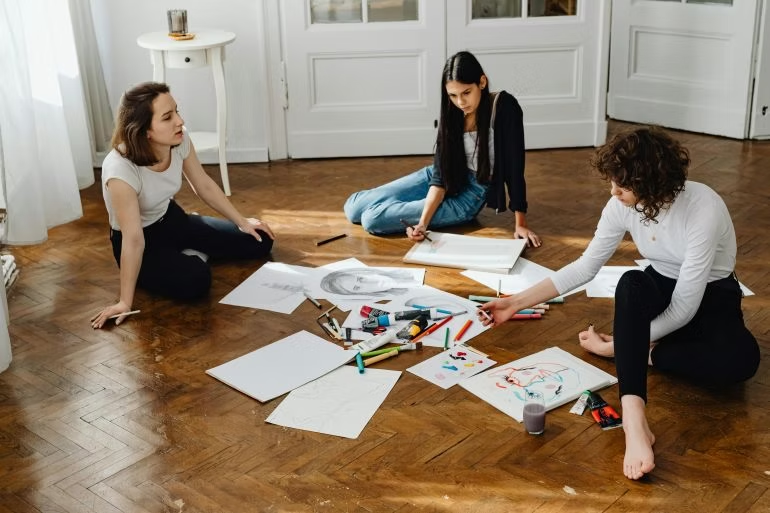 Three people sitting on the floor sketching and using art supplies together to connect

through shared creativity.