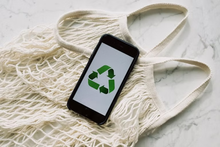 A white bag and a phone with a green recycle sign on the screen.