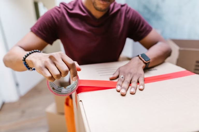 Man taping a cardboard box with red tape.