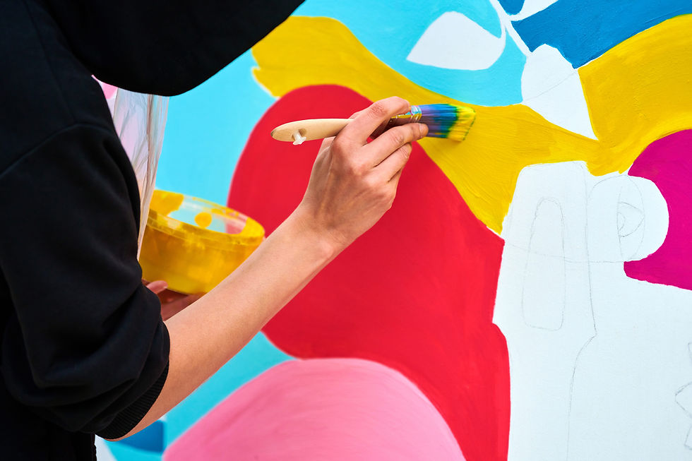 Person painting a colorful mural with a brush, applying yellow paint on a blue and red background. A vibrant, creative scene.