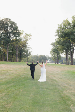 A bride and groom walk down the lawn of a golf course, with the hands in the air.