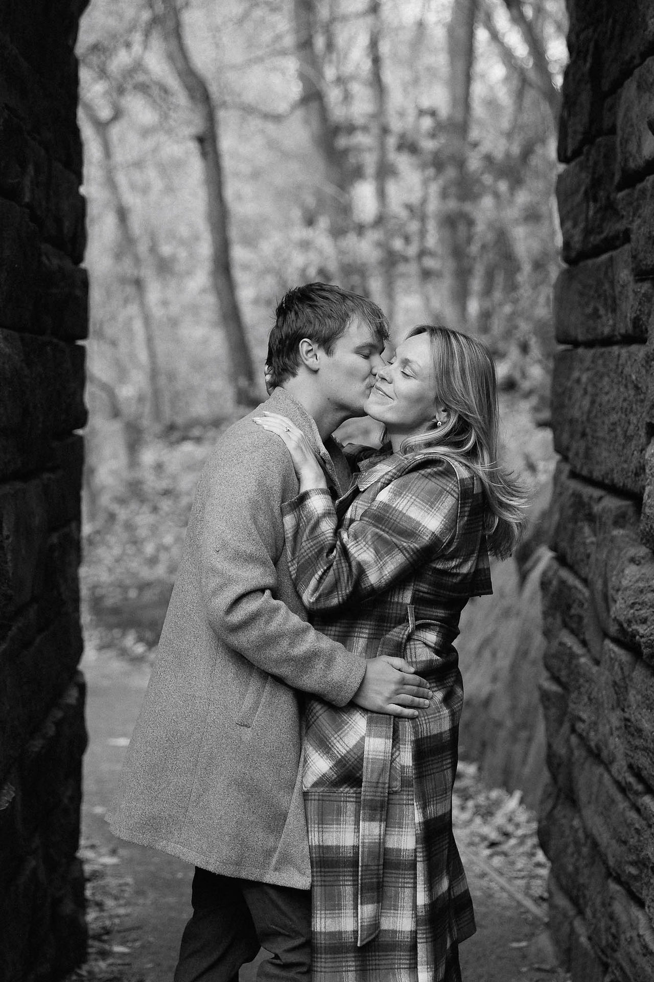 A man kisses his fiancé's cheek under the Ramble Stone Arch in Central Park.