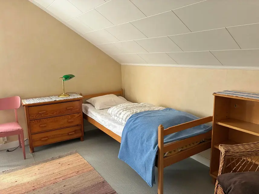 Bedroom with single bed, wooden furniture and pink chair – sleeping quarters for long stay guests