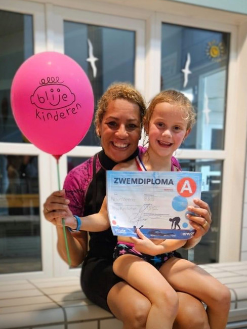 Juf Joan en leerling op schoot. Trots na behalen zwemdiploma met roze Blije Kinderen ballon