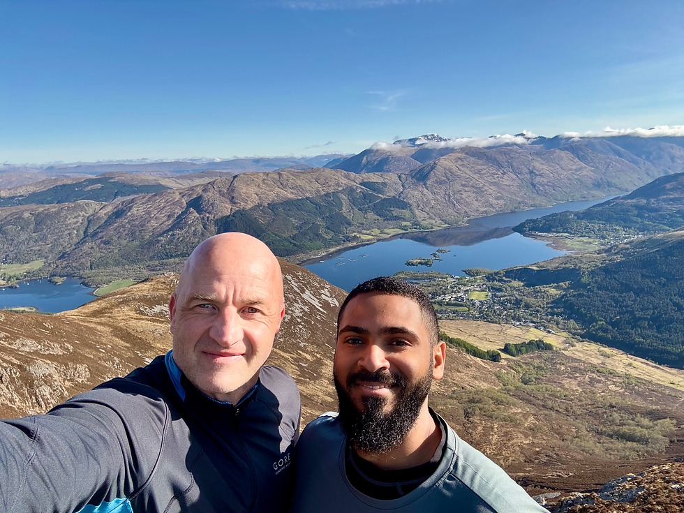 Aaron and Abdulaziz enjoying a breathtaking mountain view with a stunning loch below under a clear blue sky.