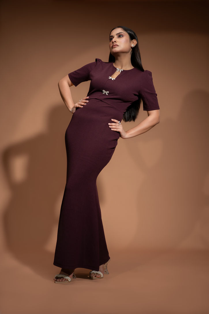 High-contrast, full-length editorial fashion shot of a model in a textured plum mermaid gown, showcasing architectural posing and dramatic studio lighting for commercial apparel advertising.