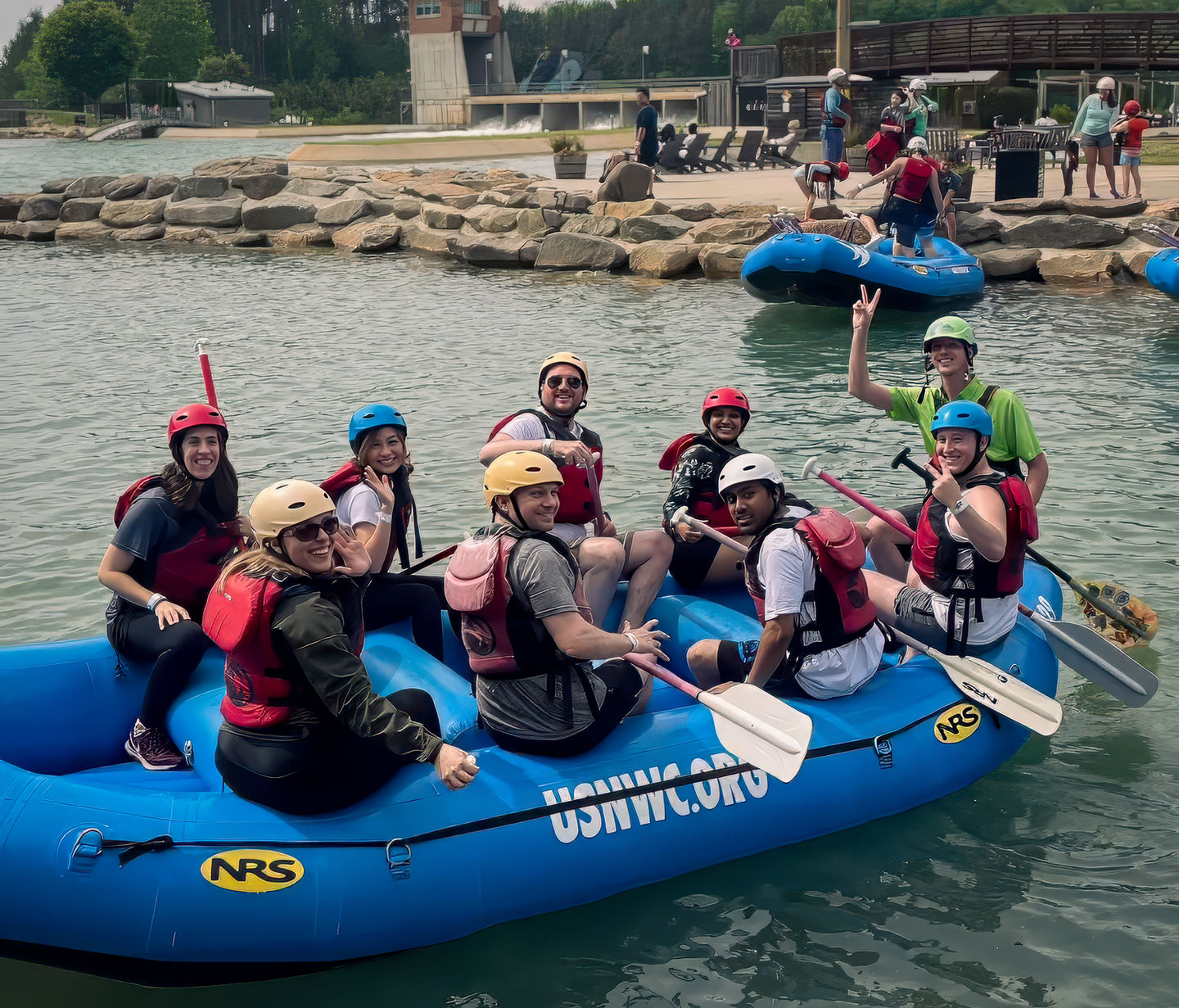 Members rafting together on a scenic river, wearing helmets and life jackets.