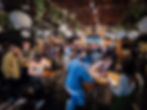 A lively social event with people mingling and conversing under decorative hanging lanterns in a stylish venue, showcasing a vibrant community gathering.