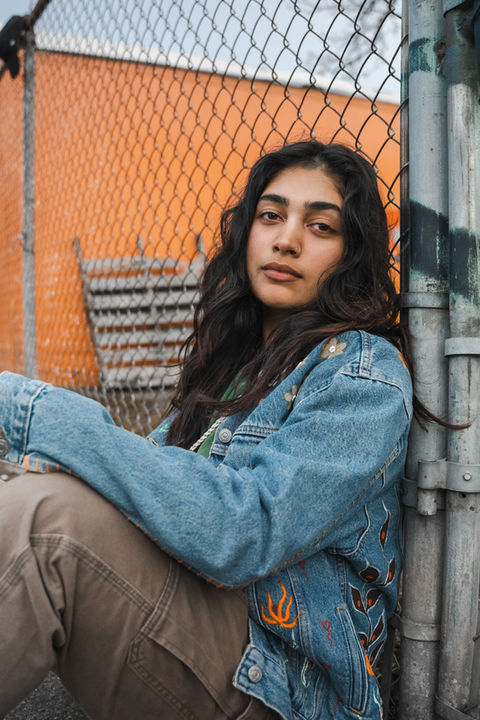 A young woman siting against a fence. 