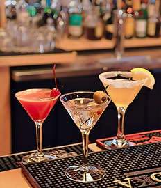 A showcase of three cocktails in martini glasses, made at Grampy's Nevada, with a bar in the background.