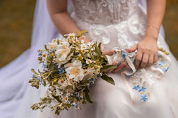 Bouquet com flores brancas e azuis nas mãos da noiva em renda, captado durante a cerimónia numa quin