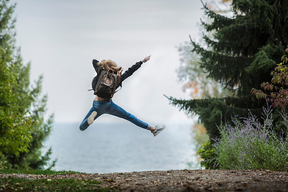Hiking woman jumping high with backpack on and excited