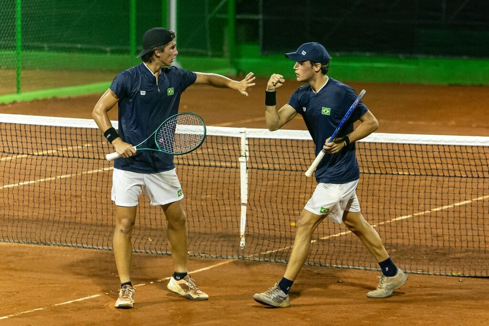 Dois tenistas com uniformes azul e branco cumprimentam-se em quadra de saibro. Ambos seguram raquetes e estão diante da rede. Leonardo Storck e Pedro Chabalgoity (Foto: Bruno Ruas/COB)