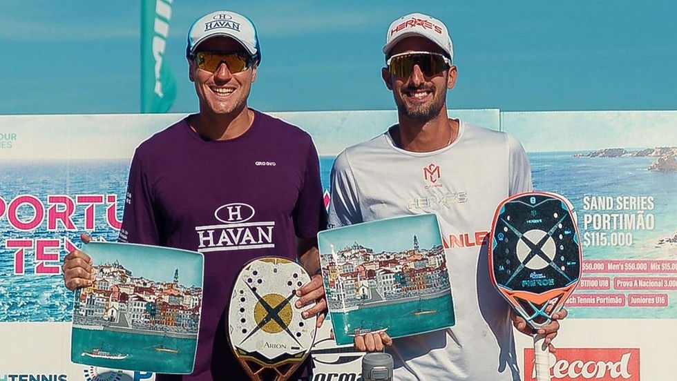 Dois homens sorridentes com raquetes e placas no Sand Series Portimão, diante do mar, com logos Havan e Herkes.