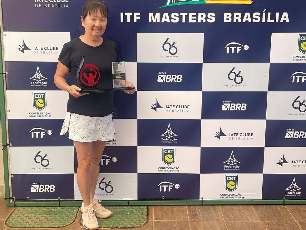 Mulher sorridente segura troféu em frente a painel com logos do Iate Clube e ITF Masters Brasília. Ela veste preto e branco.