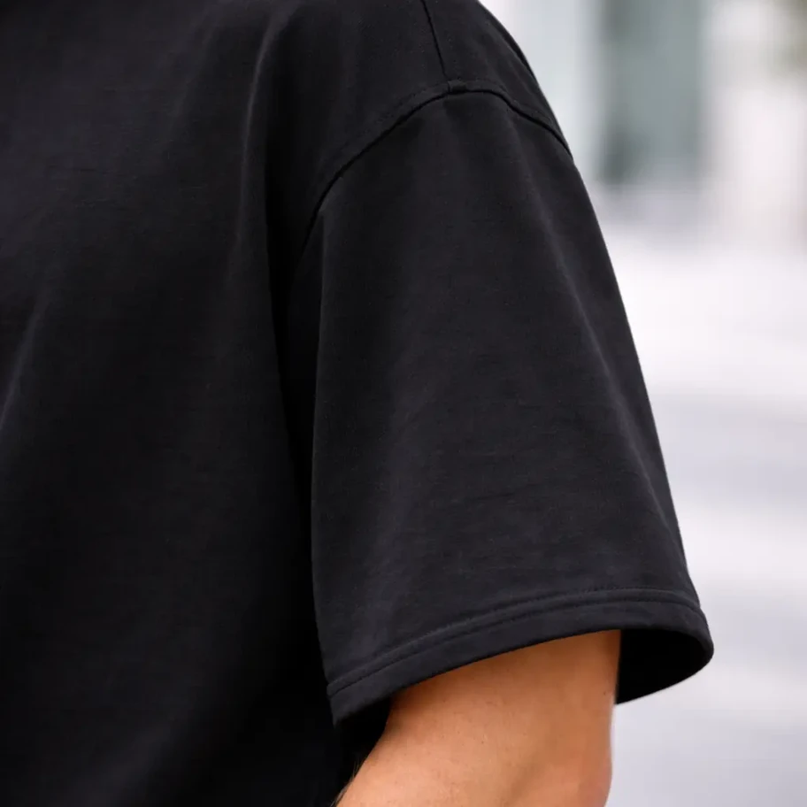 Person's shoulder and arm wearing a black oversize t-shirt outdoors.