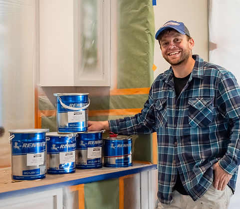The owner smiling next to paint cans in a kitchen