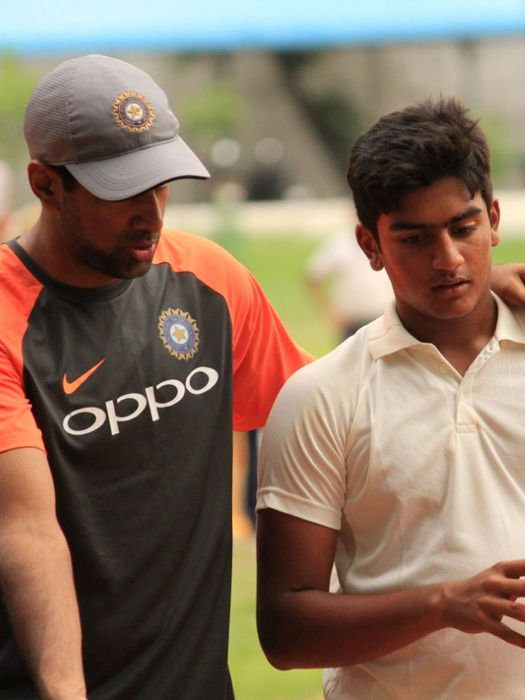 Ravichandran Ashwin placing a hand on a young cricketer’s shoulder, sharing guidance on the field