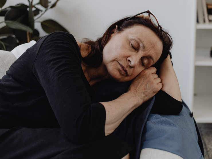 Tired woman resting on a sofa with eyes closed, representing burnout from overgiving and people pleasing.