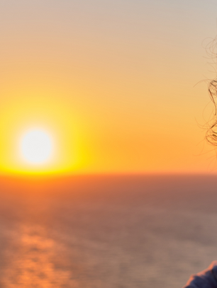A thoughtful woman looking out at a sunrise over the sea, symbolising emotional readiness, new beginnings, and the decision to start therapy.