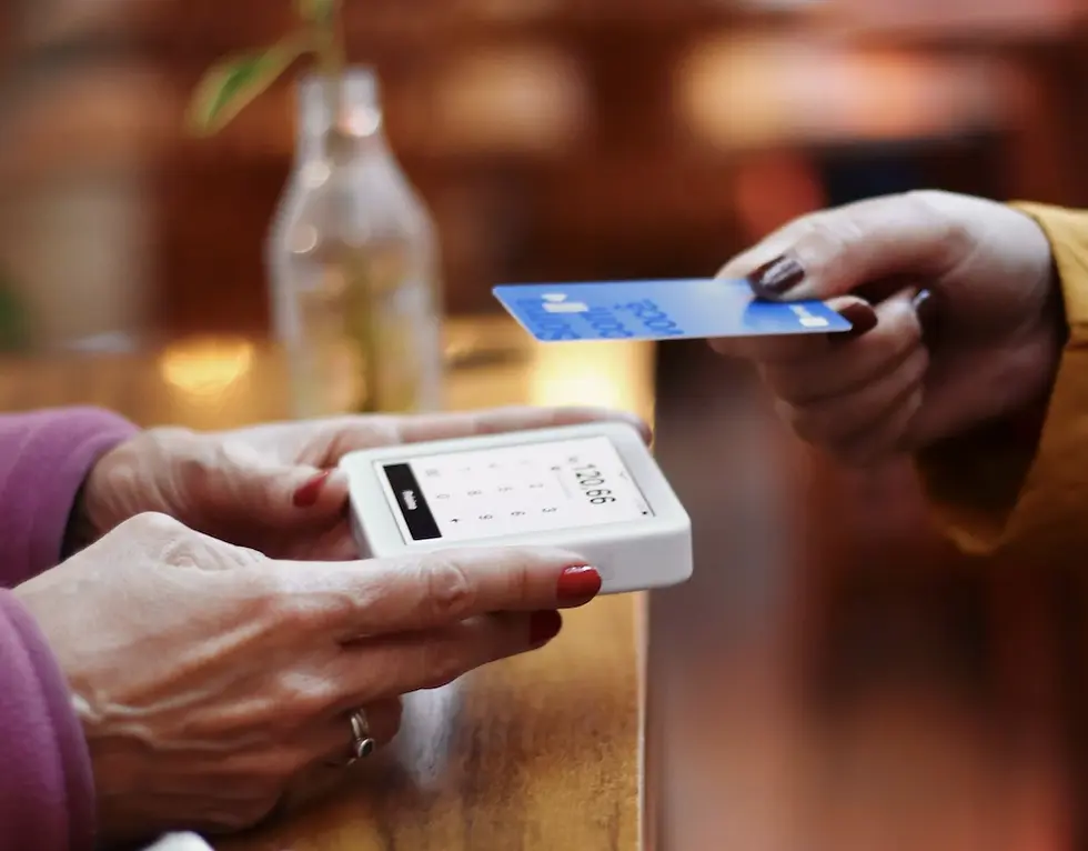 Customer tapping a contactless bank card on a handheld card reader at a charity shop counter.