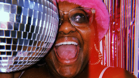 A black woman with a large smile posing next to a disco ball at a vintage party