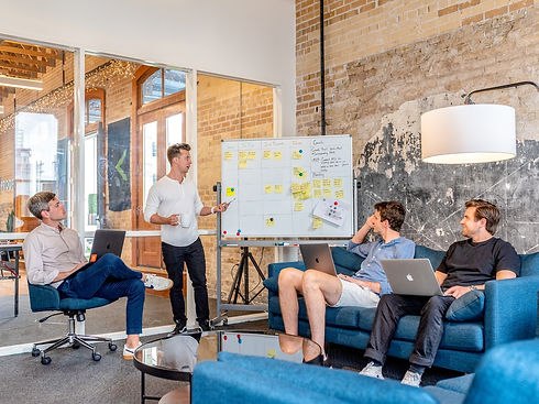 4 men in a meeting looking at a whiteboard covered in post it notes