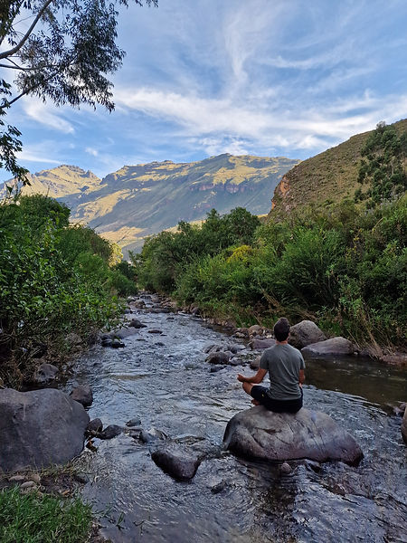 Shamanic practitioner from Full Circle Healing meditating on a rock in a tranquil Peruvian river surrounded by lush greenery