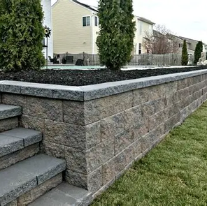 Stone retaining wall with steps in a landscaped backyard with green grass.