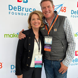 Ann with DeBruce Foundation and tom with Make48 standing next to each other smiling in front of debruce foundation step and repeat banner