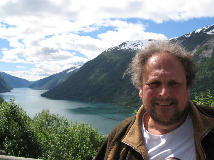 A person smiling with a scenic mountain background.