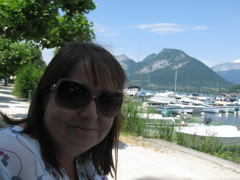 Woman wearing sunglasses by a marina with mountains.