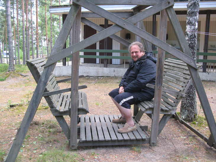 Man sitting on a wooden outdoor swing structure.