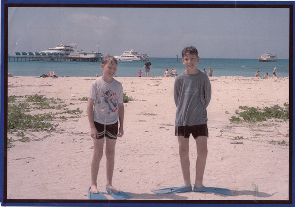Two people standing on a beach with boats behind.