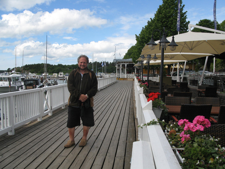 Man standing on a wooden boardwalk by the water.
