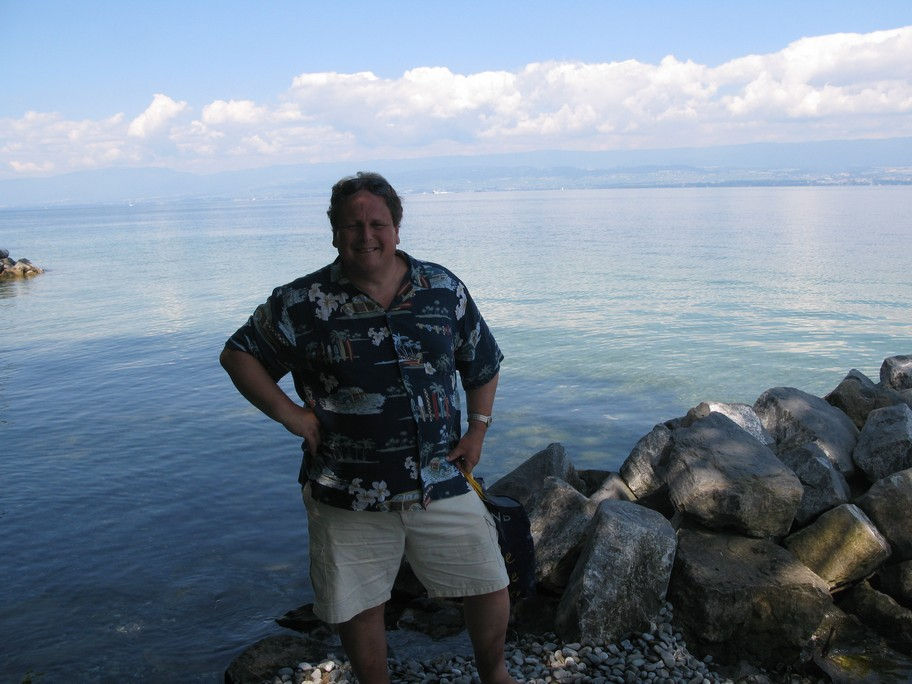 Man standing by a rocky lakeside, wearing casual clothes.
