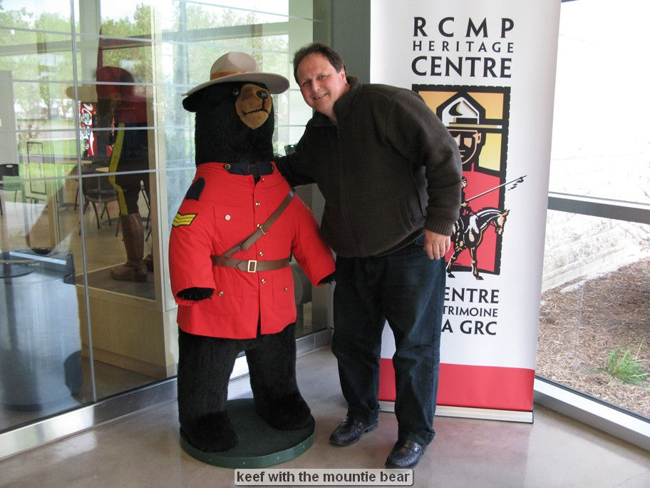 Man posing with Mountie bear statue indoors.