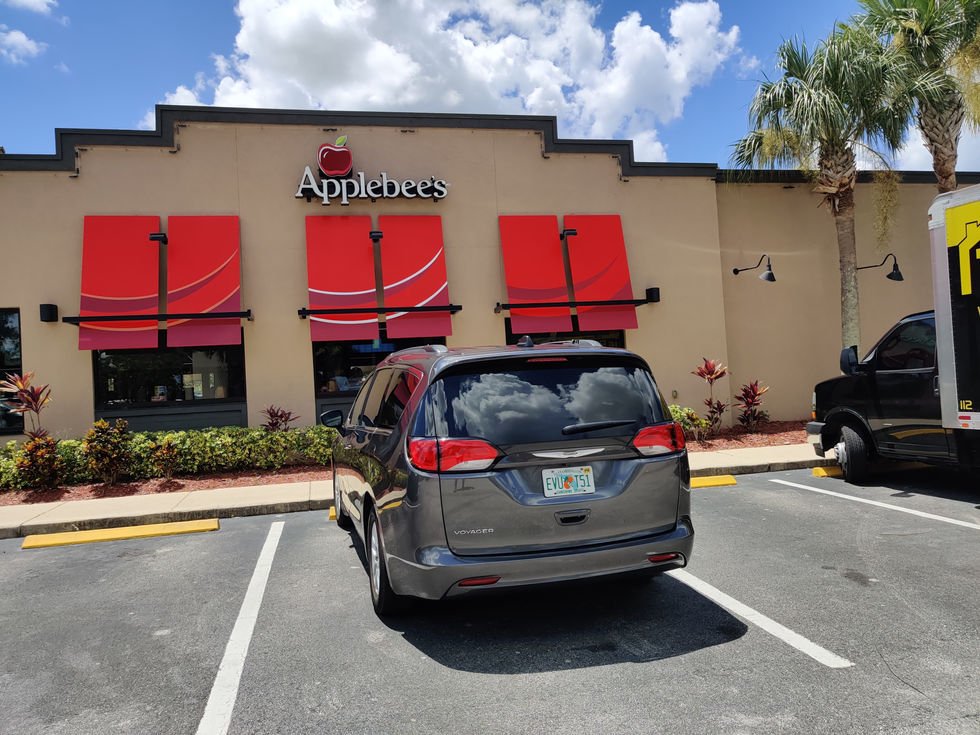 Restaurant exterior with parked cars and red awnings.