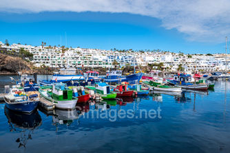 A vibrant photographic print capturing the charm of the old town harbour of Puerto del Carmen in Lanzarote, Canary Islands. Traditional fishing boats, painted in bright colours, rest peacefully on the water, reflecting the harbour’s authentic character and timeless beauty.