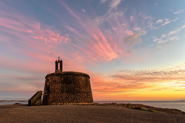 The sunset behind Castillo del Águila o de las Coloradas, this is the proper name for the small castle that looks out towards the south of the island of Lanzarote from Playa Blanca and is positioned on a small point of rock.